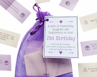 May include: A purple organza gift bag filled with small, folded paper notes. A tag reads "A Gift of Positivity, Laughter and Inspiration on your 21st Birthday." Scattered notes with inspirational quotes and small icons surround the bag.