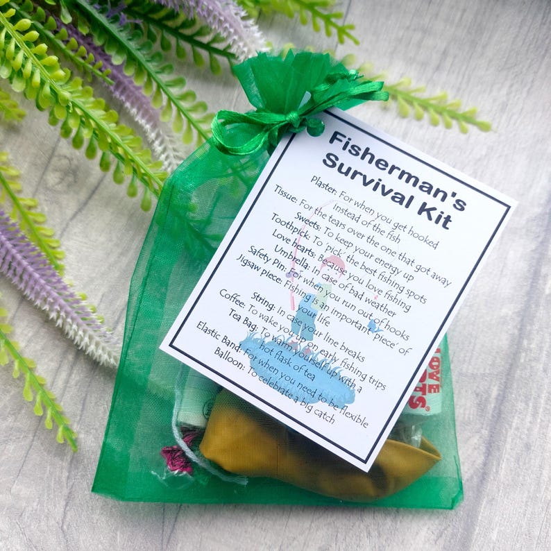 K&ouml;nnte beinhalten: Eine gr&uuml;ne Organza-Tasche gef&uuml;llt mit einem Angler-&Uuml;berlebenskit. Das Kit enth&auml;lt ein Taschentuch, einen Zahnstocher, S&uuml;&szlig;igkeiten, Herzchen, eine Sicherheitsnadel, ein Puzzle-Teil, Schnur, Kaffee, einen Teebeutel, ein Gummiband und einen Ballon. An der Tasche ist eine wei&szlig;e Karte mit dem Text "Fisherman's Survival Kit" und einer Liste der Artikel und ihrer Verwendung befestigt.