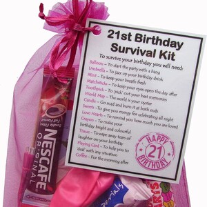 May include: A pink mesh bag filled with a 21st birthday survival kit. The kit includes a balloon, umbrella, mint, matchsticks, toothpick, world map, candle, sweets, love hearts, crayon, tissue, playing card, and coffee. The bag has a tag that reads "21st Birthday Survival Kit" and lists the items included in the kit.