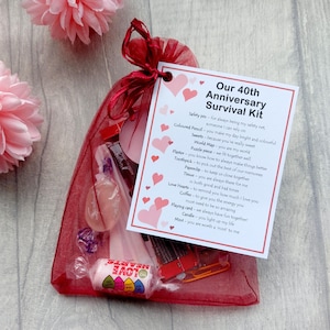 May include: A red organza bag filled with small gifts and a card that reads "Our 40th Anniversary Survival Kit". The card lists items like a safety pin, coloured pencil, sweets, world map, puzzle piece, plaster, toothpick, paperclip, tissue, love hearts, coffee, playing card, candle, and mint.
