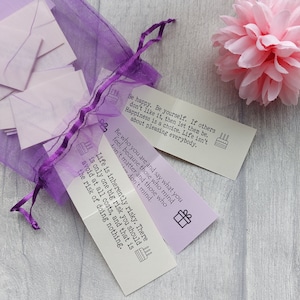 May include: A set of purple and white cards with inspirational quotes printed on them. The quotes include "Be happy. Be yourself. If others don't like it, then let them be. Happiness is a choice. Life isn't about pleasing everybody." and "Life is inherently risky. There is only one big risk you should avoid at all costs, and that is the risk of doing nothing."