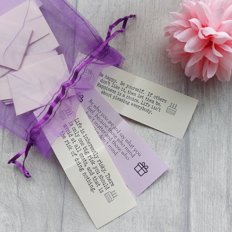 May include: A set of purple and white cards with inspirational quotes printed on them. The quotes include "Be happy. Be yourself. If others don't like it, then let them be. Happiness is a choice. Life isn't about pleasing everybody." and "Life is inherently risky. There is only one big risk you should avoid at all costs, and that is the risk of doing nothing."