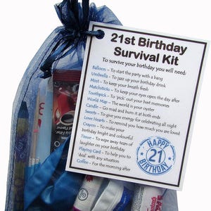 May include: A blue and white gift bag filled with a 21st birthday survival kit. The bag contains a balloon, a candle, a pack of matches, a world map, a pack of love hearts, a crayon, a tissue, a playing card, and a coffee packet. The bag has a tag attached that reads "21st Birthday Survival Kit" and lists the contents of the bag with a description of how to use each item.