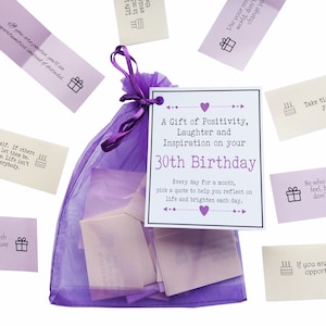 May include: A purple organza bag filled with small white cards. The bag has a white card attached to it with the text "A Gift of Positivity, Laughter and Inspiration on your 30th Birthday. Every day for a month, pick a quote to help you reflect on life and brighten each day."