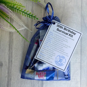 Puede incluir: Una bolsa de organza azul llena de un kit de supervivencia para un 30 cumplea&ntilde;os. El kit incluye un globo, un paraguas, menta, cerillas, un palillo de dientes, un mapa del mundo, una vela, dulces, corazones de amor, un cray&oacute;n, un pa&ntilde;uelo, una carta de juego y caf&eacute;. La bolsa tiene una etiqueta adjunta con el texto "Kit de supervivencia para un 30 cumplea&ntilde;os" y una lista de los art&iacute;culos necesarios para sobrevivir al cumplea&ntilde;os.
