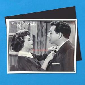 May include: Black and white photo of a couple, a woman with short dark hair and a man with dark hair, wearing a suit and tie. The photo has the text "Perry & Della" at the top.