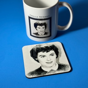 May include: A white ceramic mug with a black and white photo of Della Street on it. The mug has a black handle and the text "Della Street" printed on the front. A black and white coaster with a photo of Della Street is also included.
