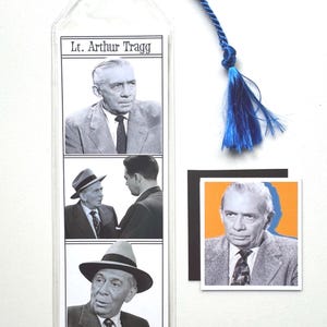 May include: A bookmark with three black and white images of a man in a suit, with the text "Lt. Arthur Tragg". A blue tassel is attached to the top. A small square image of the man is also included.