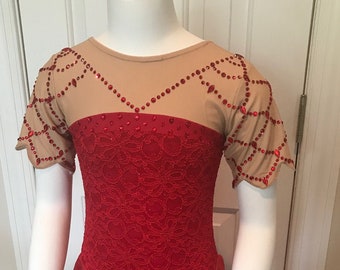 Op de afbeelding: Een rode kunstschaatsjurk met een beige mesh juk en mouwen. Het lijfje is versierd met rood kant en strass. De rok is van vloeiende rode chiffon. De jurk wordt gepresenteerd op een mannequin.