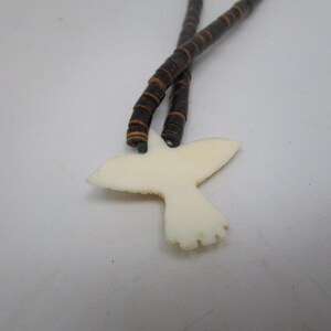 May include: A white bird pendant with brown and black beaded necklace.