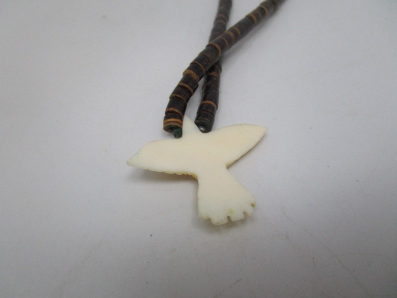 May include: A white bird pendant with brown and black beaded necklace.