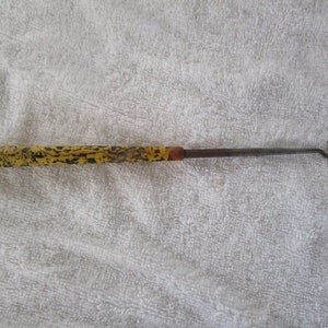 May include: A yellow and black patterned metal hook with a metal handle. The hook is used for pulling items out of tight spaces.