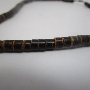 May include: A close-up of a necklace made of dark brown wooden beads. The beads are cylindrical and have a slightly rough texture.