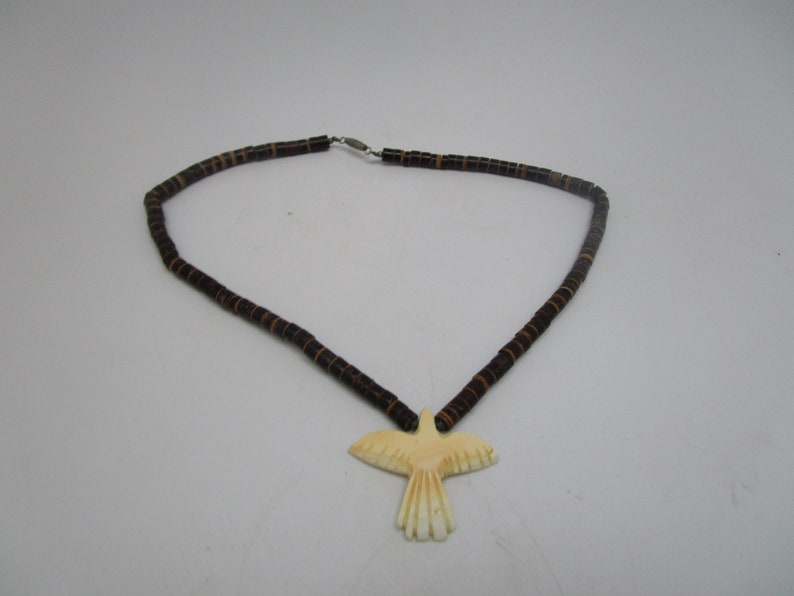 May include: A brown beaded necklace with a carved bone bird pendant. The bird is white with a light brown color on the wings.