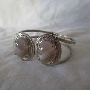 May include: A silver bangle bracelet with two oval-shaped agate stones. The stones are a light gray with white and brown stripes.