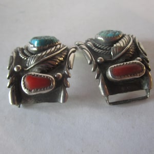 May include: A pair of silver watch band clasps with turquoise and coral stones. The clasps are intricately designed with feather motifs.