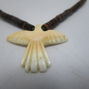 May include: A necklace with a carved bird pendant made of white shell. The necklace is made of brown wooden beads.