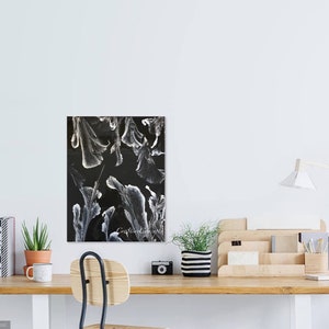 May include: Abstract painting with white and black paint on a black canvas. The white paint is in the shape of swirls and lines. The painting is framed and hanging on a white wall.