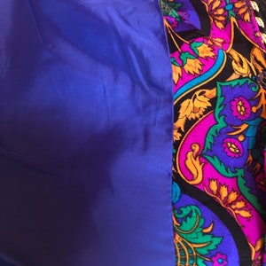May include: Close-up of a jacket interior. The lining is a solid royal blue, contrasting with the patterned exterior. The exterior features a paisley design in shades of purple, black, gold, and green.