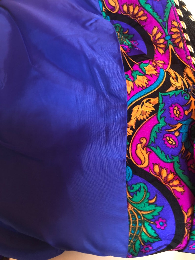 May include: Close-up of a jacket interior. The lining is a solid royal blue, contrasting with the patterned exterior. The exterior features a paisley design in shades of purple, black, gold, and green.