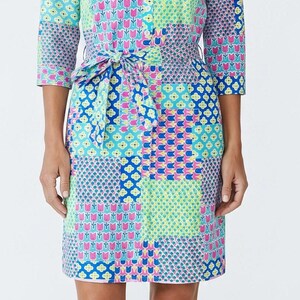 May include: A knee-length shirt dress featuring a vibrant patchwork pattern in shades of bright blue, lime green, and hot pink. The dress has three-quarter length sleeves, a collared neckline, a button-down front, and a matching fabric tie-waist belt.