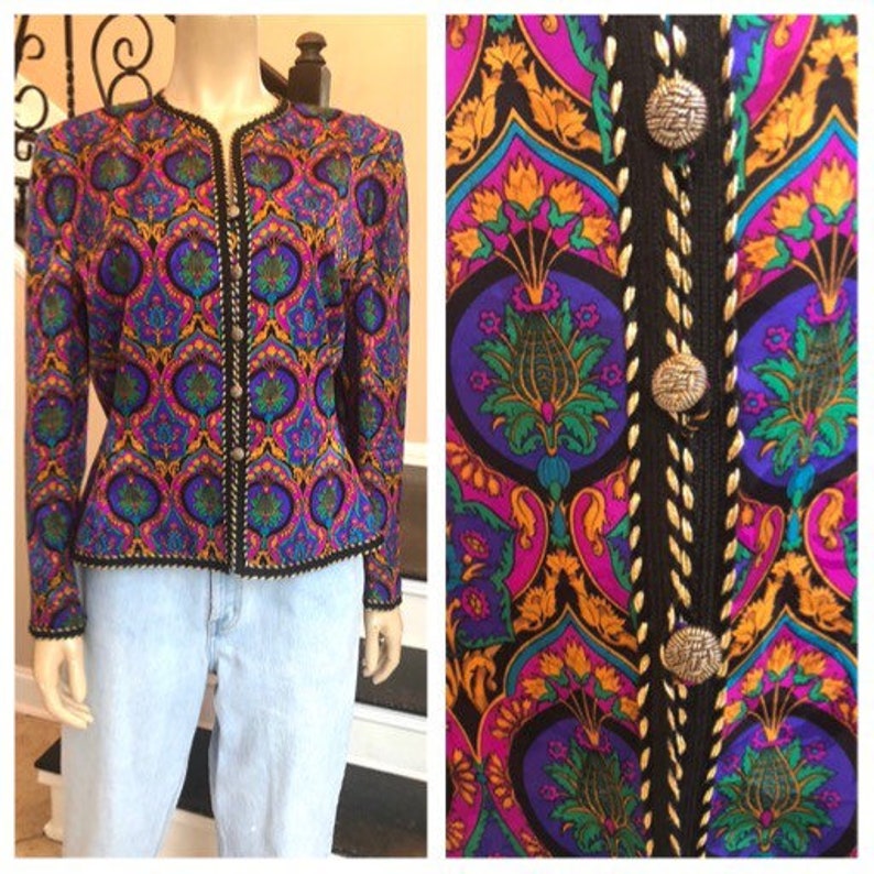 May include: A vibrant, patterned jacket in shades of purple, teal, and gold. The jacket features a detailed floral design and is accented with black trim and decorative buttons. The jacket is displayed on a mannequin with light blue jeans.