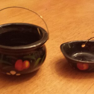 May include: Two small black ceramic pots with gold wire handles. Both pots have a red, yellow, and green floral design.