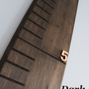 Pu&ograve; includere: Un grafico di crescita in legno marrone scuro con linee nere e numeri. Il numero "5" &egrave; visibile sul grafico.