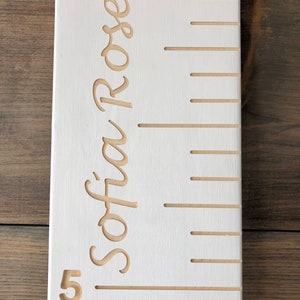 May include: White wooden growth chart with a ruler and the name "Sofia Rose" engraved in cursive.