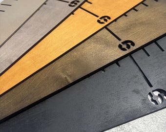 May include: A set of five flat wooden rulers arranged in a fan shape, featuring varying wood stain finishes including light gray, medium brown, golden yellow, dark brown, and black. Each ruler displays laser-cut markings and the number 6.
