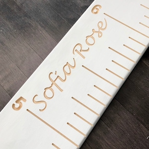 May include: White wooden growth chart with a gold inscription that reads "Sofia Rose" and a number "5" at the bottom.