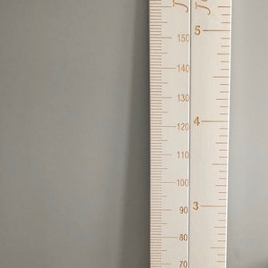 May include: White wooden growth chart with gold lettering. The chart has measurements in inches from 30 to 190. The names "Jason" and "Jaime" are written on the chart.