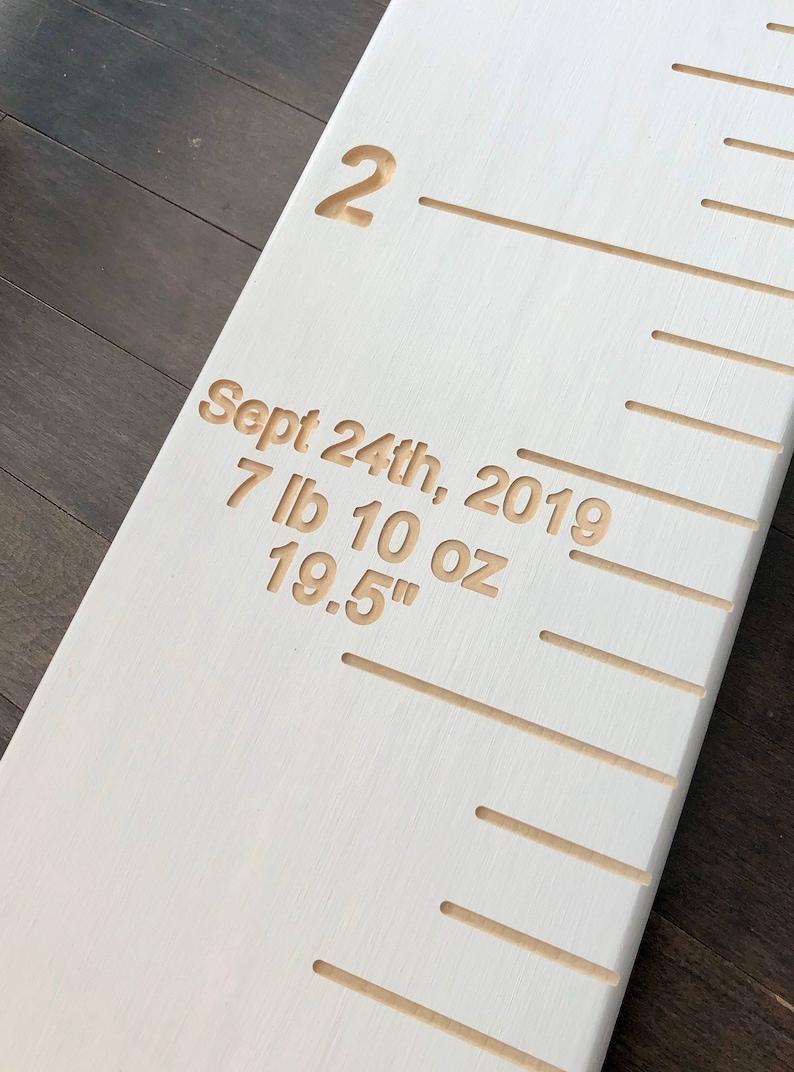 May include: White wooden growth chart with a ruler and markings for measuring height. The chart has a date, weight, and height inscription: "Sept 24th, 2019, 7 lb 10 oz, 19.5" "