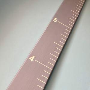 May include: A gray wooden ruler with white markings and gold numbers. The ruler is marked with numbers 4, 5, and 6.