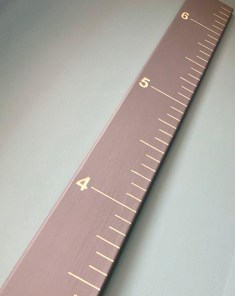 May include: A gray wooden ruler with white markings and gold numbers. The ruler is marked with numbers 4, 5, and 6.