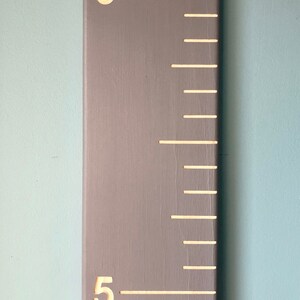 May include: A gray wooden growth chart with white markings and numbers. The numbers 5 and 6 are visible on the chart.