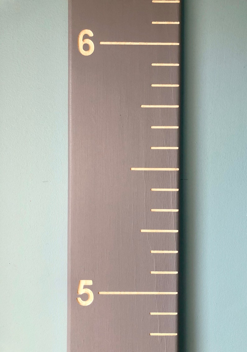 May include: A gray wooden growth chart with white markings and numbers. The numbers 5 and 6 are visible on the chart.