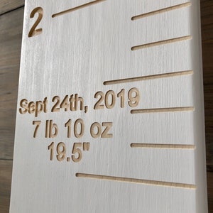 May include: White wooden growth chart with a ruler marked in inches. The chart has a date of "Sept 24th, 2019" and measurements of "7 lb 10 oz" and "19.5" inches.