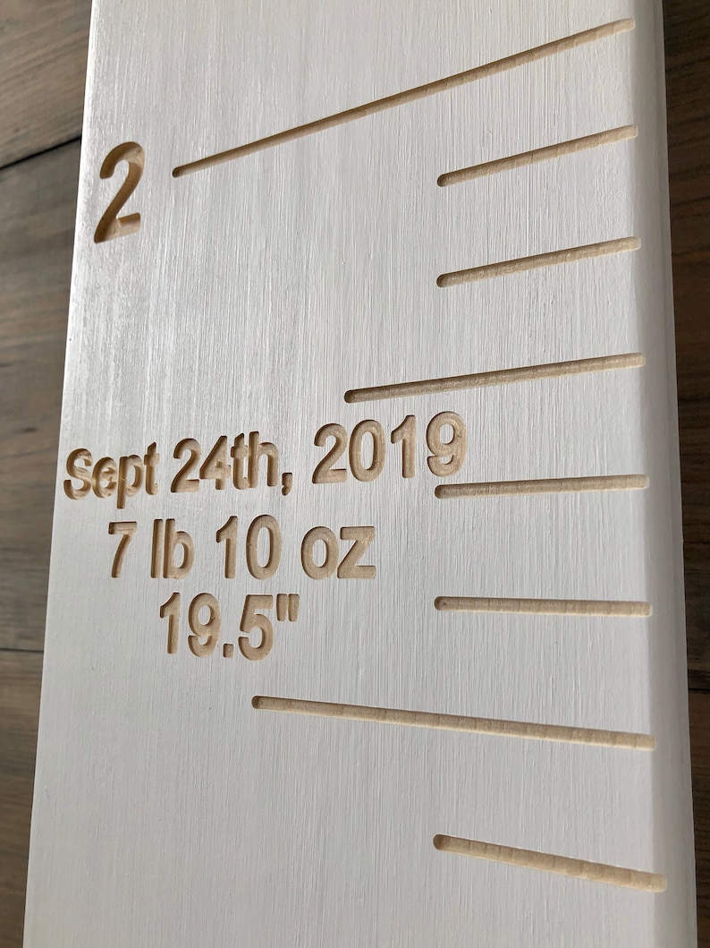 May include: White wooden growth chart with a ruler marked in inches. The chart has a date of "Sept 24th, 2019" and measurements of "7 lb 10 oz" and "19.5" inches.