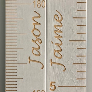 May include: White wooden growth chart with a ruler on the left side and two names on the right side. The names are "Jason" and "Jaime" and the numbers on the ruler go up to 180.