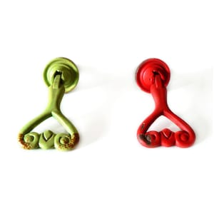 Könnte beinhalten: Zwei antike Schrankknöpfe mit herzförmigem Design. Ein Knopf ist grün und der andere rot lackiert.