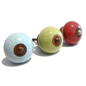 Può includere: Tre pomelli in ceramica con finitura smaltata craquelé. I pomelli sono in tonalità di blu, verde e rosso. Ogni pomello ha un accento in ottone al centro.
