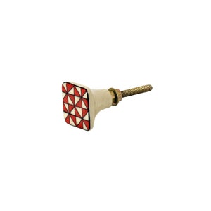 May include: A square cabinet knob with a cream base and a geometric pattern of red and white triangles. It features a brass-coloured metal screw for attachment. The design is modern and decorative.