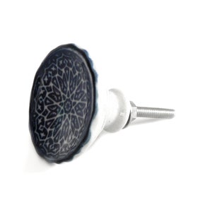 May include: A decorative cabinet knob with a dark blue and white geometric design. The knob has an oval shape with a white base and a silver screw. The pattern is intricate and symmetrical. Ideal for furniture.