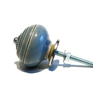 May include: A light blue ceramic cabinet knob with a silver screw and washer. The knob has a striped design.