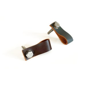 May include: Two leather drawer pulls with a metal screw. One pull is brown leather and the other is grey leather.