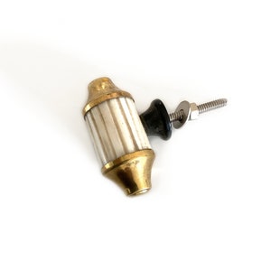 May include: A brass and white cabinet knob with a black plastic base and a silver screw. The knob has a fluted design.