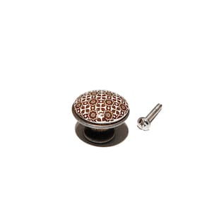 Könnte beinhalten: Ein brauner und weißer Keramik-Schrankknopf mit einem dekorativen Blumenmuster. Der Knopf wird mit einer silbernen Schraube geliefert.