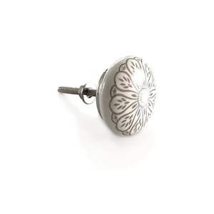 Könnte beinhalten: Weißer Keramik-Knopf mit braunem Blumenmuster. Der Knopf hat eine silberne Schraube.