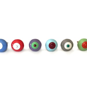 Könnte beinhalten: Satz von sechs bunten runden Knöpfen mit einem weißen Mittelkreis und einem kleineren farbigen Kreis in der Mitte. Die Knöpfe sind aus Holz und haben eine glänzende Oberfläche.